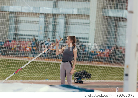 Pole vaulting indoors - young pretty woman standing near the mat in the stadium Pole vaulting indoors - young pretty woman standing near the mat in the stadium 59363073