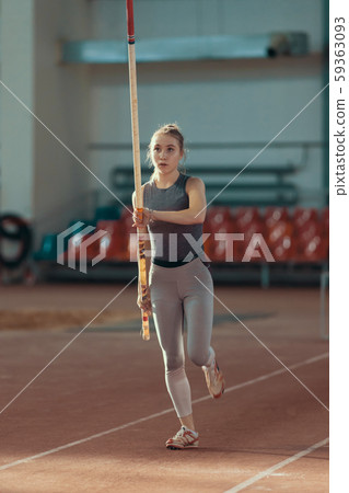 Pole vaulting indoors - young sportive woman running with a pole in her hands 59363093