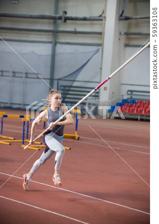 Pole vaulting indoors - young woman in leggins running with a pole in the hands Pole vaulting indoors - young woman in leggins running with a pole in the hands 59363108