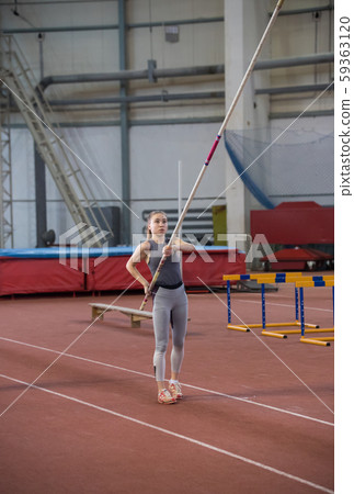Pole vaulting indoors - young woman holding a pole looking up on it Pole vaulting indoors - young woman holding a pole looking up on it 59363120