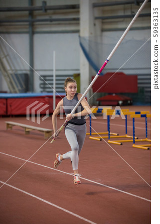 Pole vaulting indoors - young sportive woman running on the runway with a pole in the hands Pole vaulting indoors - young sportive woman running on the runway with a pole in the hands 59363135