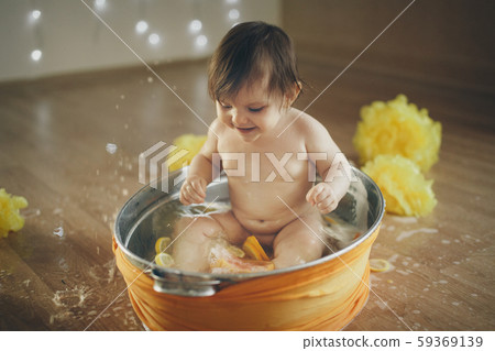 A little girl is bathing in a bath with lemon and grapefruit. A child washes in a basin among yellow A little girl is bathing in a bath with lemon and grapefruit. A child washes in a basin among yellow 59369139