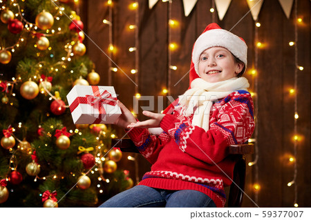 Cheerful santa helper girl with gift box sitting Cheerful santa helper girl with gift box sitting 59377007
