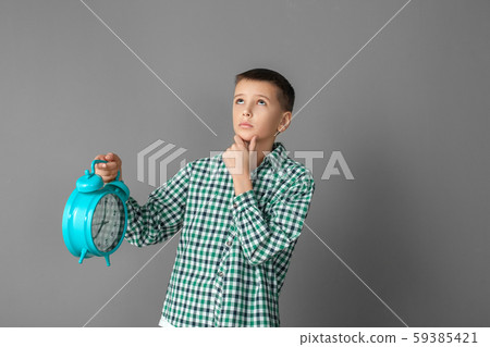 Freestyle. Boy standing isolated on grey wall with alarm clock looking up pensive 59385421