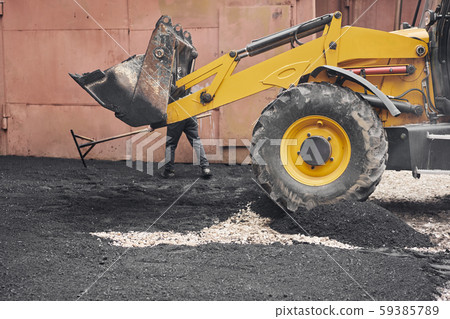 A tractor unloads the asphalt. Large heavy machinery is carrying out road repair work. Laying new A tractor unloads the asphalt. Large heavy machinery is carrying out road repair work. Laying new 59385789