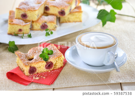 Delicious cuts of cherry cake with icing sugar and mint leaves served with a cappuccino 59387538