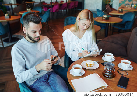 Casual guy scrolling in gadget while his girlfriend making notes or sketch 59390814
