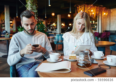 Serious guy scrolling in smartphone while his girlfriend making notes in notepad 59390816