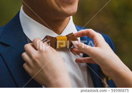 Caring bride straightening wooden bow tie to groom 59390875