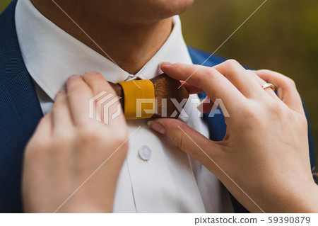 Caring bride straightening wooden bow tie to groom 59390879