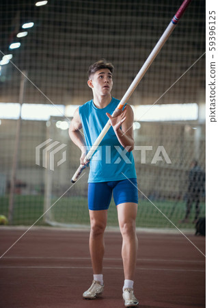Pole vaulting - young guy in a blue suit is rising in hands a pole Pole vaulting - young guy in a blue suit is rising in hands a pole 59396125