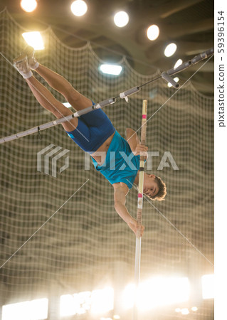 Pole vaulting - guy is jumping over the bar holding on to a pole 59396154