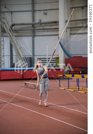 Pole vaulting - woman in gray shirt is going to run with a long pole in her hands Pole vaulting - woman in gray shirt is going to run with a long pole in her hands 59396371