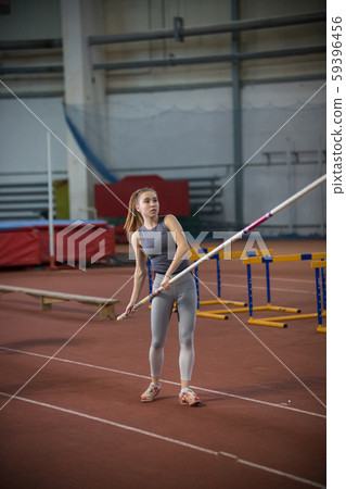 Pole vaulting - young woman is standing with pole in hands 59396456