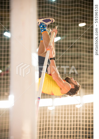 Pole vaulting in the sports stadium - an athletic man jumping over the bar with his legs up Pole vaulting in the sports stadium - an athletic man jumping over the bar with his legs up 59396538