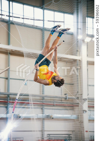 Pole vaulting indoors - a athletic man jumping over the bar - leaning on the pole Pole vaulting indoors - a athletic man jumping over the bar - leaning on the pole 59396602