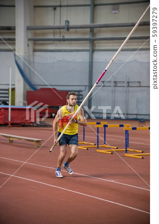 Pole vaulting indoors - a man in yellow shirt about to run up on the track with a pole Pole vaulting indoors - a man in yellow shirt about to run up on the track with a pole 59397279