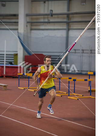 Pole vaulting indoors - a man in yellow shirt running on the track with a pole in the stadium Pole vaulting indoors - a man in yellow shirt running on the track with a pole in the stadium 59397280