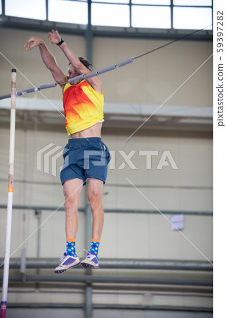 Pole vaulting indoors - a man falling down after jumping over the bar Pole vaulting indoors - a man falling down after jumping over the bar 59397282