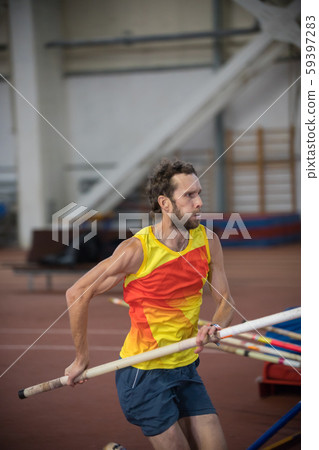 Pole vaulting indoors - an athletic man running on the track with a pole Pole vaulting indoors - an athletic man running on the track with a pole 59397283