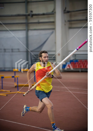 Pole vaulting indoors - a man running on the track with a pole in the stadium Pole vaulting indoors - a man running on the track with a pole in the stadium 59397300