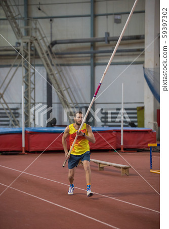 Pole vaulting indoors - a man in yellow shirt standing on the track with a pole Pole vaulting indoors - a man in yellow shirt standing on the track with a pole 59397302