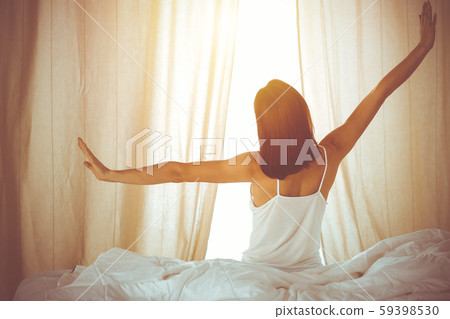 Woman stretching hands in bed after wake up, sun flare . Brunette entering a day happy and relaxed 59398530