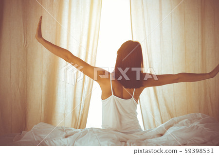 Woman stretching hands in bed after wake up, sun flare . Brunette entering a day happy and relaxed Woman stretching hands in bed after wake up, sun flare . Brunette entering a day happy and relaxed 59398531
