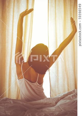 Woman stretching hands in bed after wake up, sun flare . Brunette entering a day happy and relaxed 59398549