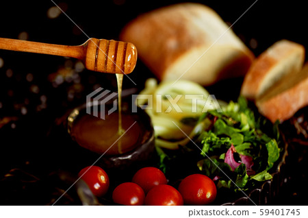 Table with delicious and nutritious food .Honey, cheese and tomatoes. Honey flows down with a wooden 59401745