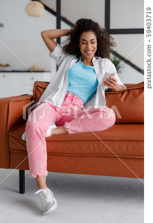 Joyful Afro American lady using smartphone at home Joyful Afro American lady using smartphone at home 59403719