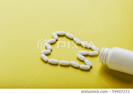 Calcium vitamin in the form of a tooth spilled out of a white jar on a yellow background. 59407231