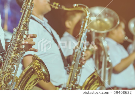 Male student with friends blow the saxophone with the band for performance on stage at night. 59408622
