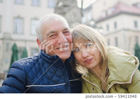 Handsome elderly man is embracing his young blonde wife spending time together outdoors in the Handsome elderly man is embracing his young blonde wife spending time together outdoors in the 59411048
