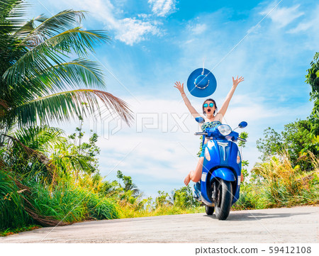 Crazy funny woman with flying hair riding a motorbike on a blue sky and green tropics background 59412108