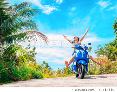 Crazy funny woman with flying hair riding a motorbike on a blue sky and green tropics background Crazy funny woman with flying hair riding a motorbike on a blue sky and green tropics background 59412119