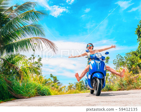 Crazy funny woman with flying hair riding a motorbike on a blue sky and green tropics background 59412135
