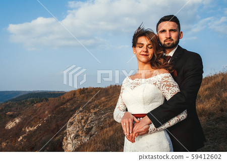 Amazing wedding couple, bride and groom holding hands on a mountains background. Cute girl in white Amazing wedding couple, bride and groom holding hands on a mountains background. Cute girl in white 59412602