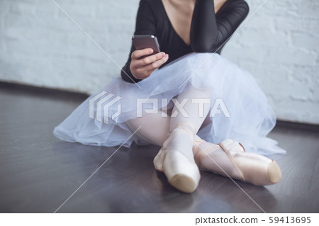 Young ballet dancer sitting leaning white wall using phone in studio active lifestyle close-up Young ballet dancer sitting leaning white wall using phone in studio active lifestyle close-up 59413695