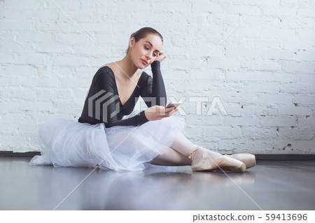 Young ballet dancer sitting leaning white wall using phone in studio active lifestyle Young ballet dancer sitting leaning white wall using phone in studio active lifestyle 59413696