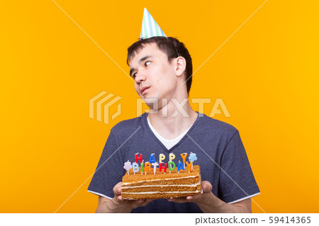 Crazy cheerful young man in glasses and paper congratulatory hats holding cakes happy birthday Crazy cheerful young man in glasses and paper congratulatory hats holding cakes happy birthday 59414365