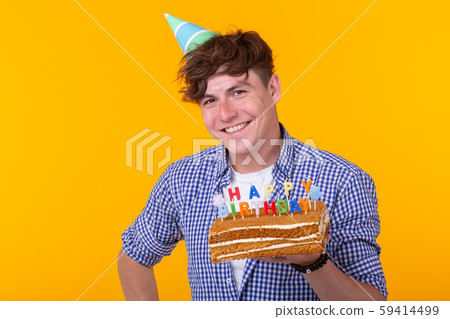 Positive young man holding a happy birthday cake posing on a yellow background. 59414499