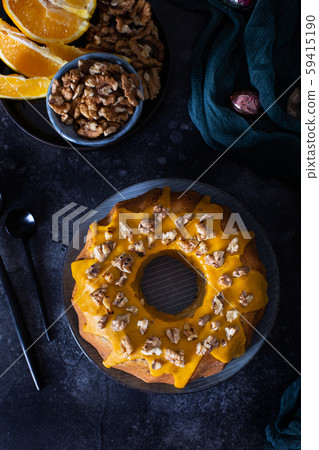 Bundt cake, orange cake with walnuts and yellow sugar icing with turmeric spice. Dark background. View from above Bundt cake, orange cake with walnuts and yellow sugar icing with turmeric spice. Dark background. View from above 59415190