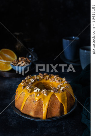 Bundt cake, orange cake with walnuts and yellow sugar icing with turmeric spice. Dark background Bundt cake, orange cake with walnuts and yellow sugar icing with turmeric spice. Dark background 59415193