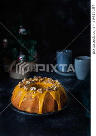 Bundt cake, orange cake with walnuts and yellow sugar icing with turmeric spice. Dark background 59415194