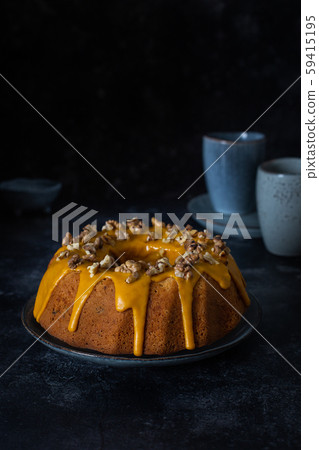 Bundt cake, orange cake with walnuts and yellow sugar icing with turmeric spice. Dark background Bundt cake, orange cake with walnuts and yellow sugar icing with turmeric spice. Dark background 59415195