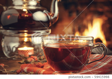 Tea with hawthorn in a glass cup and teapot with a tealight on a wooden table in a room with a Tea with hawthorn in a glass cup and teapot with a tealight on a wooden table in a room with a 59415998