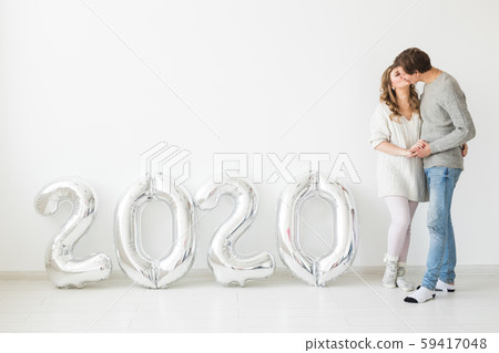 Holidays, festive and party concept - Happy loving couple near silver 2020 balloons on white 59417048