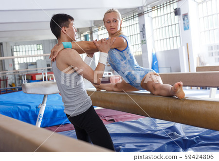 Woman in bodysuit training at broad bars in sport gym, man helping Woman in bodysuit training at broad bars in sport gym, man helping 59424806
