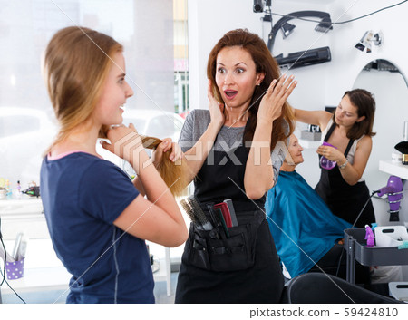 Puzzled hairstylist inspecting hair of teen girl Puzzled hairstylist inspecting hair of teen girl 59424810